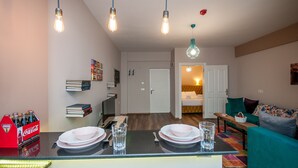 Una sala de estar moderna con sofá, comedor con mesa lista para dos personas y cocina equipada con refrigerador y microondas.