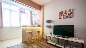 Una sala de estar moderna con televisor, taburetes de madera, una estantería y un ventanal con cortinas.