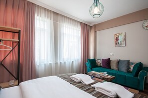 A hotel room with a bed, a sofa, a wooden side table, and a hanging light fixture. - Newway Apartments (Istanbul)