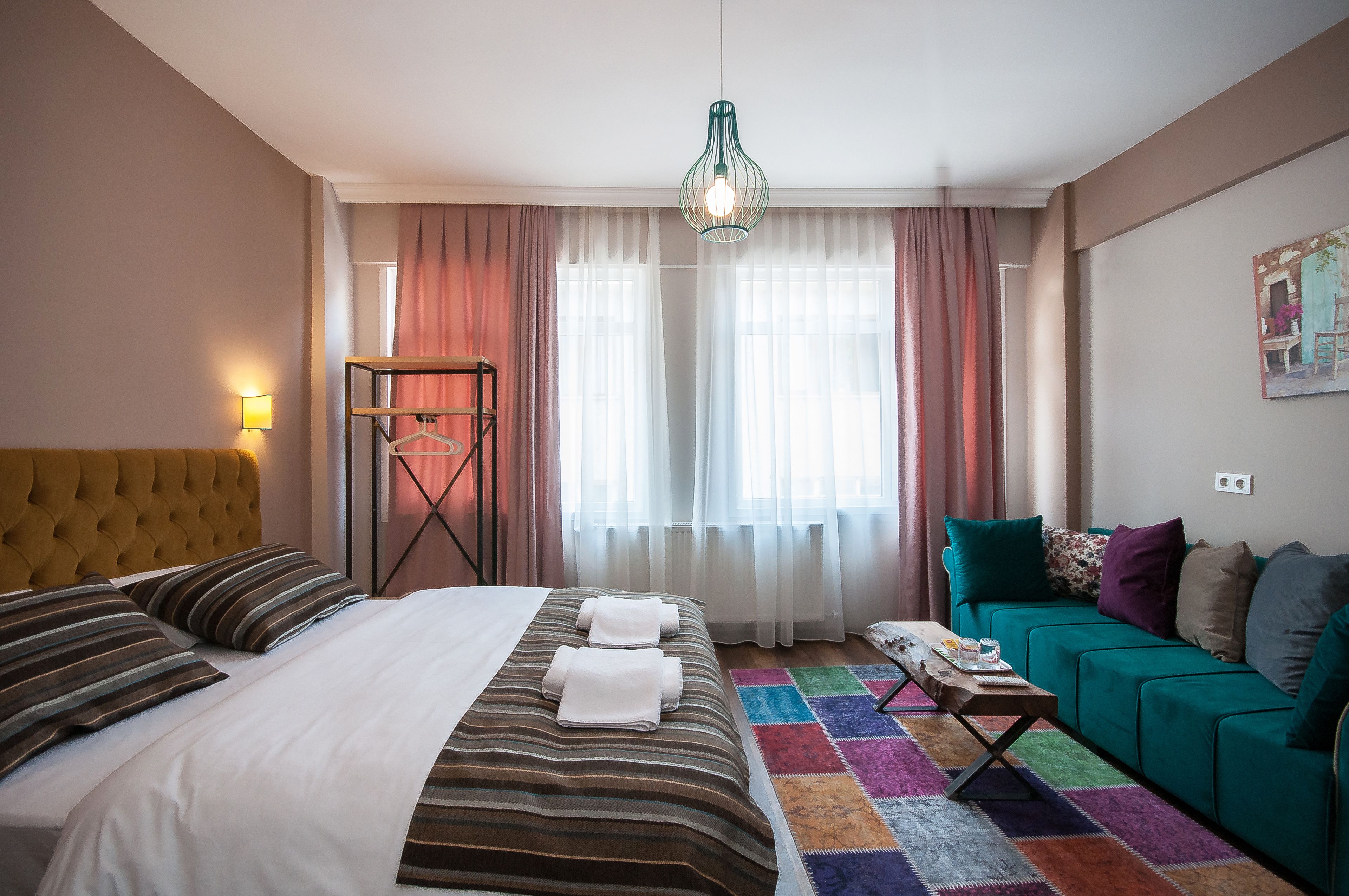A hotel room with a bed, a green sofa, a colorful rug, and a hanging light fixture.