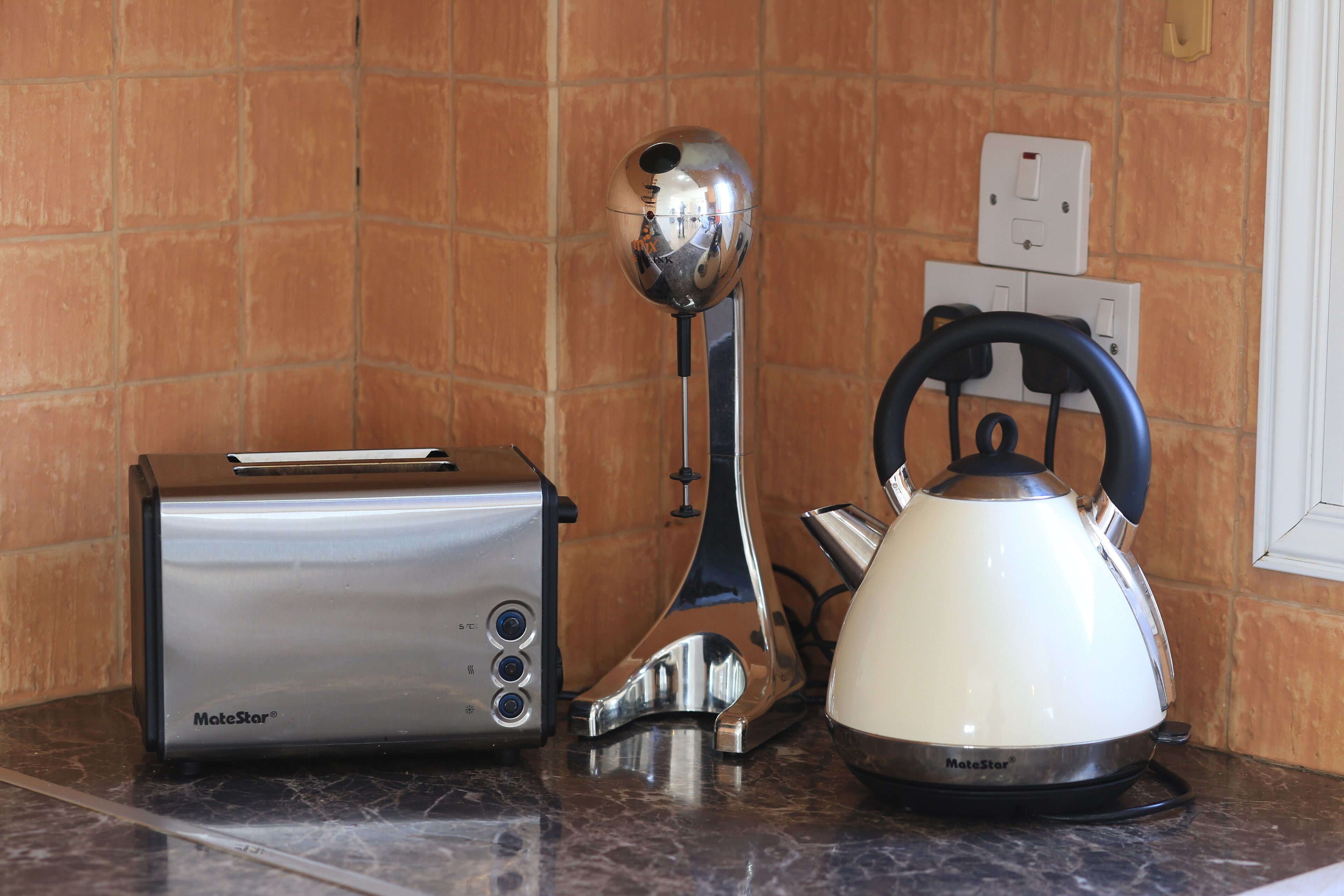 A kitchen counter with a toaster, a kettle, and a reflective object.