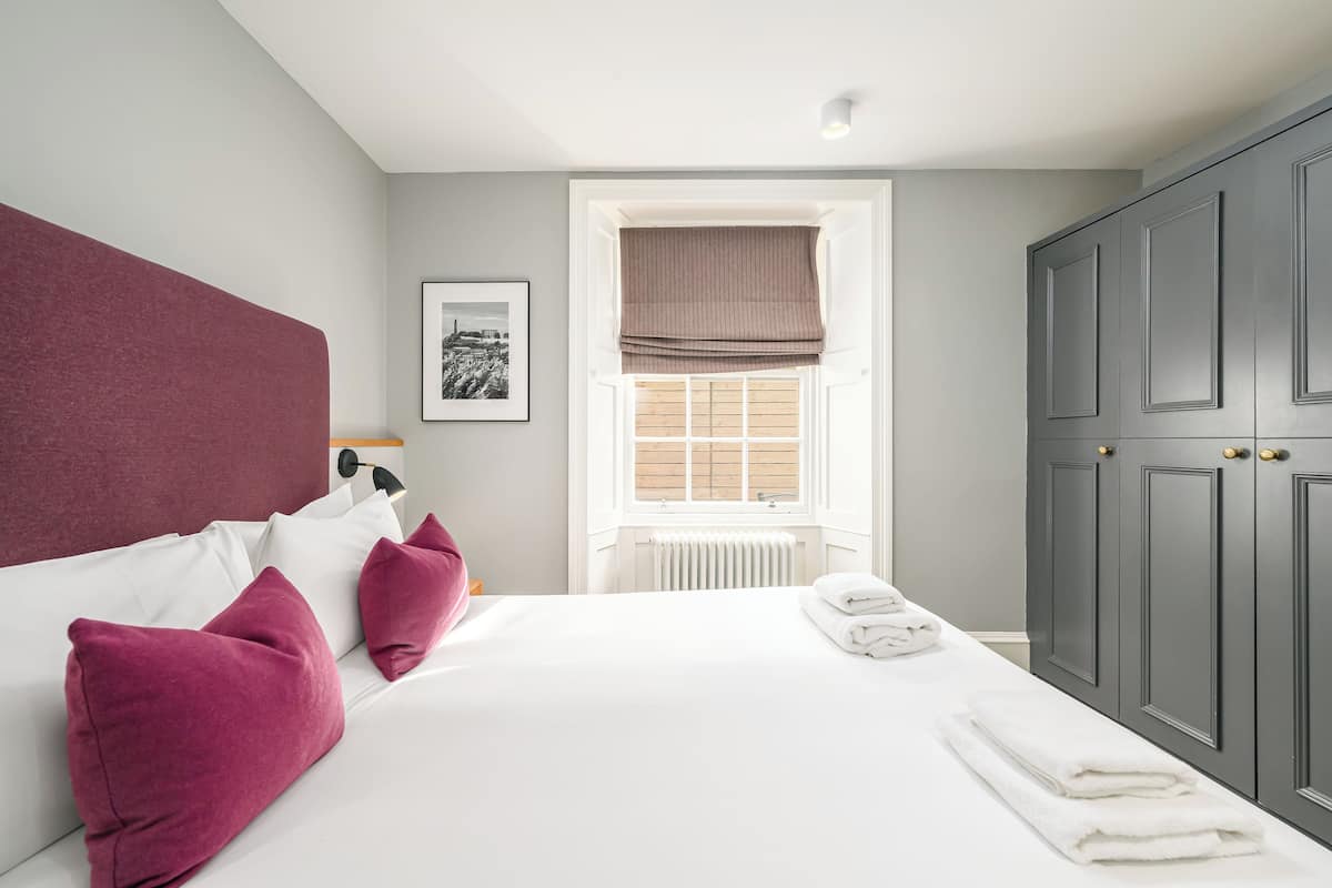 Un dormitorio con una cama grande, ropa de cama blanca y una ventana con vistas.