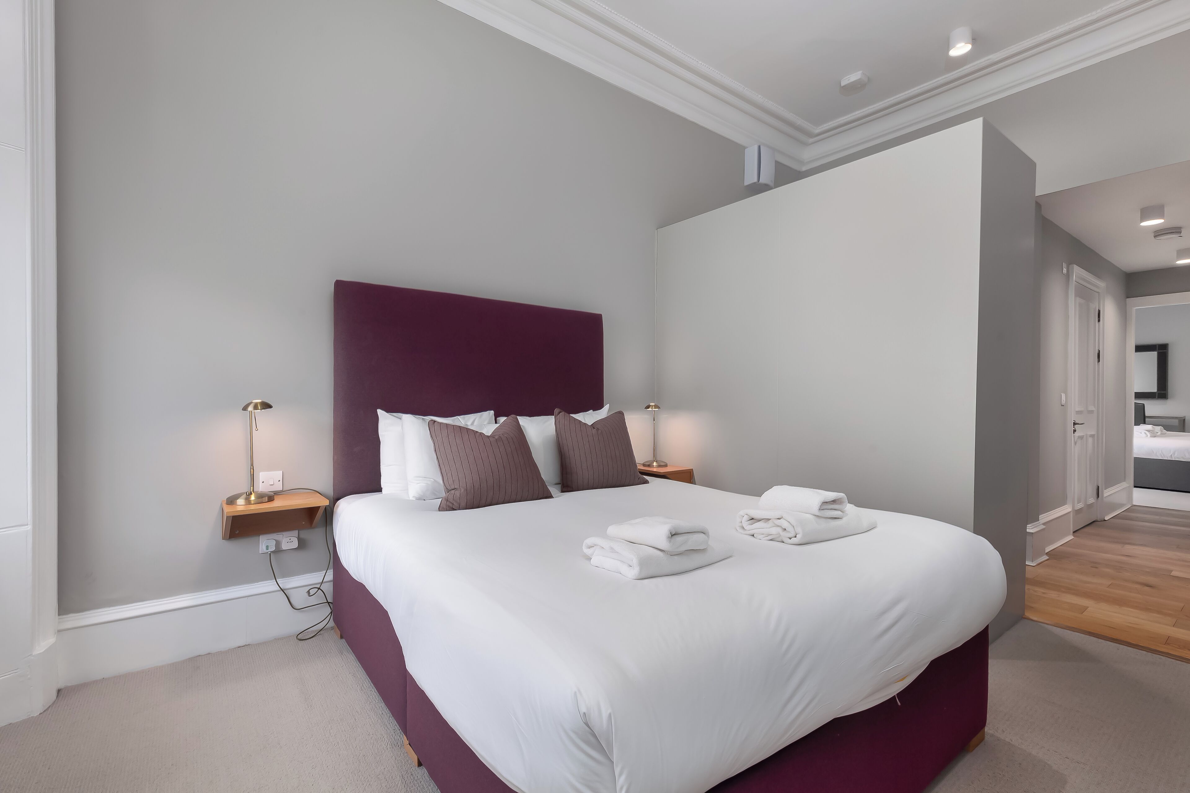 A neatly made bed with white linens and brown pillows, a wooden nightstand with a lamp, and a modern headboard.