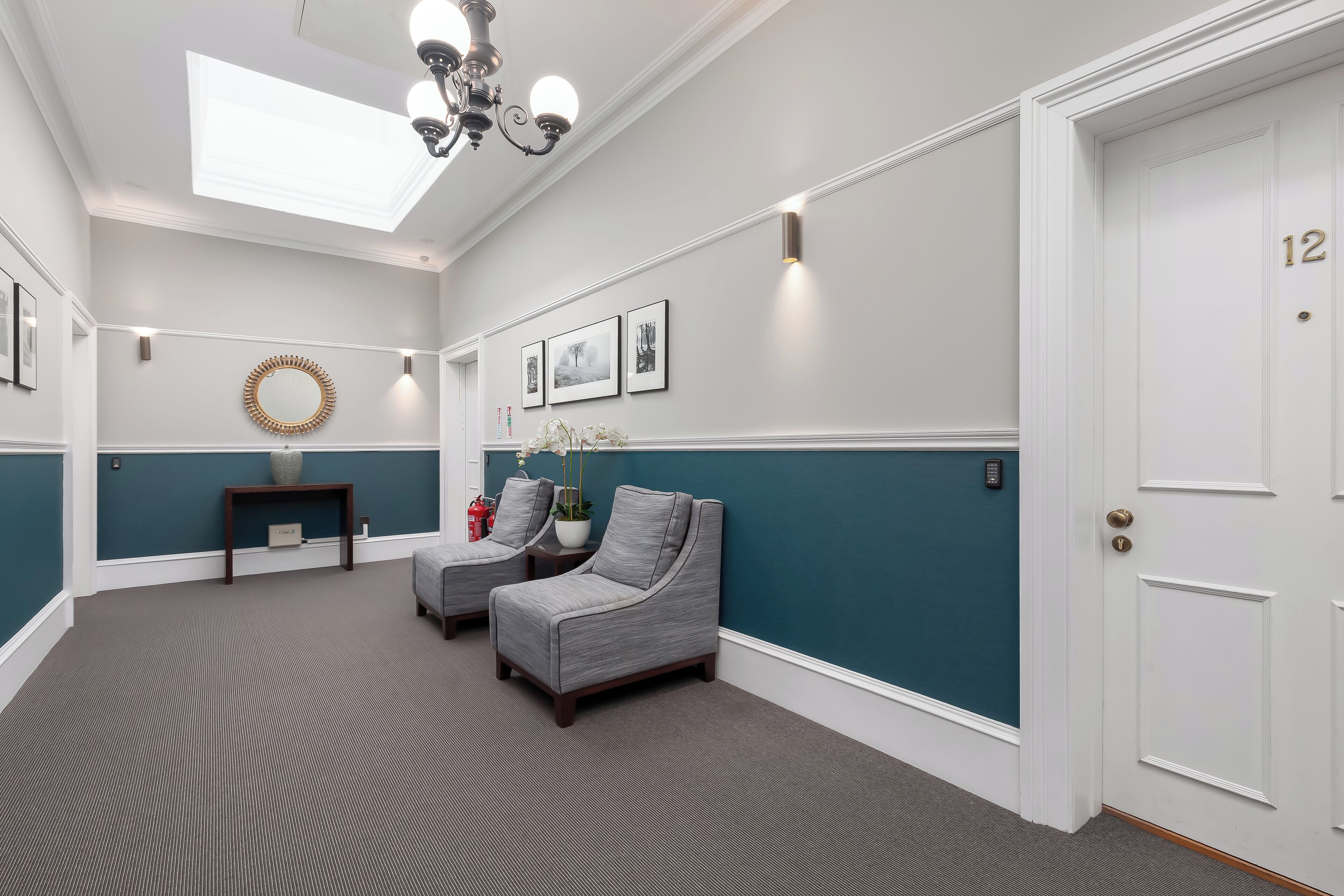 A room with two grey armchairs, a small table with a vase, a mirror, and framed pictures on the wall.