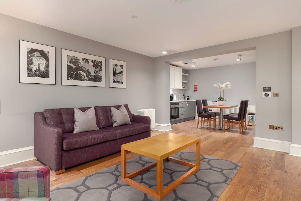 Una sala de estar moderna con un sofá morado, una mesa de centro de madera y una zona de comedor con una mesa y sillas blancas.