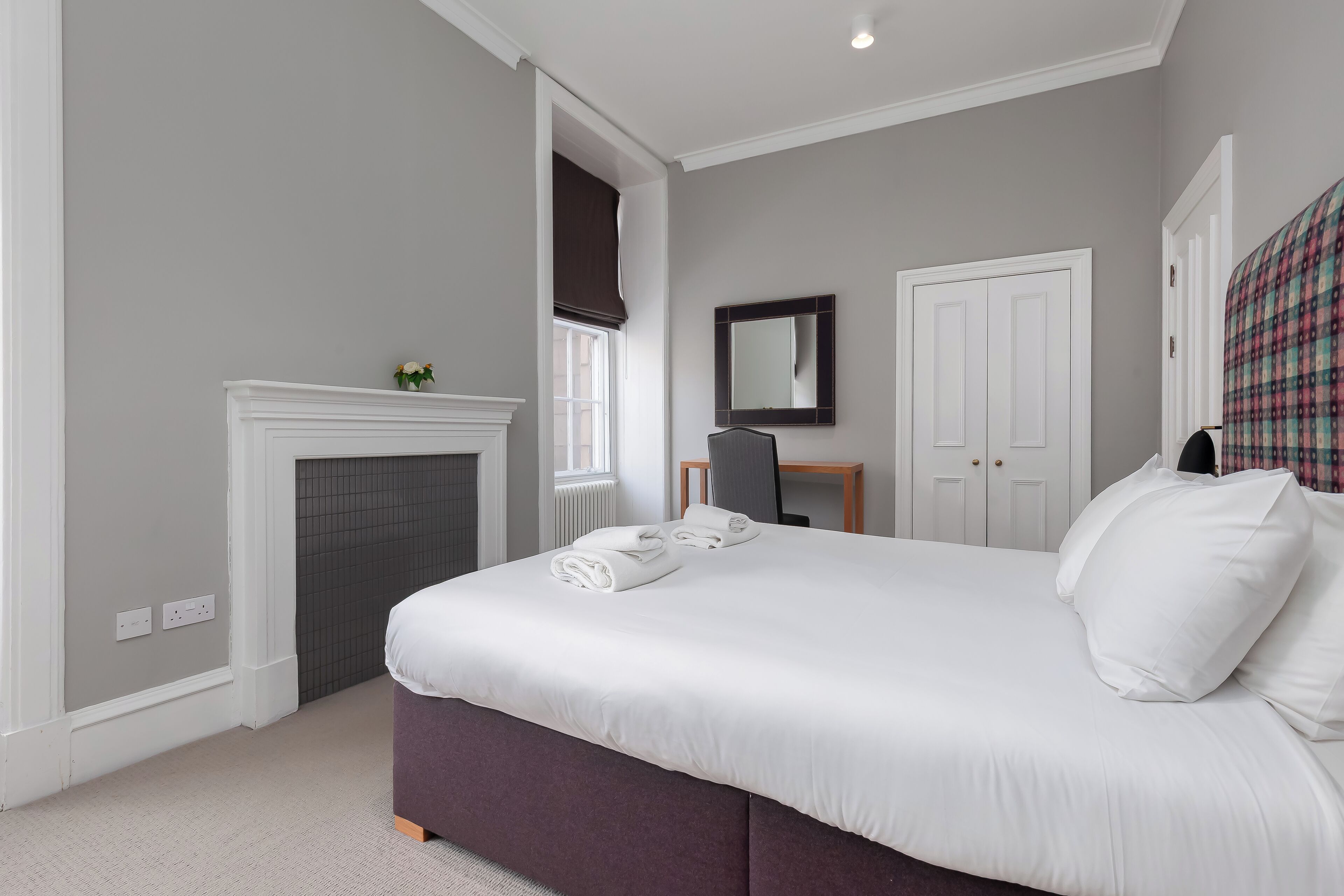A bedroom with a large bed, a fireplace, a mirror, and a door.
