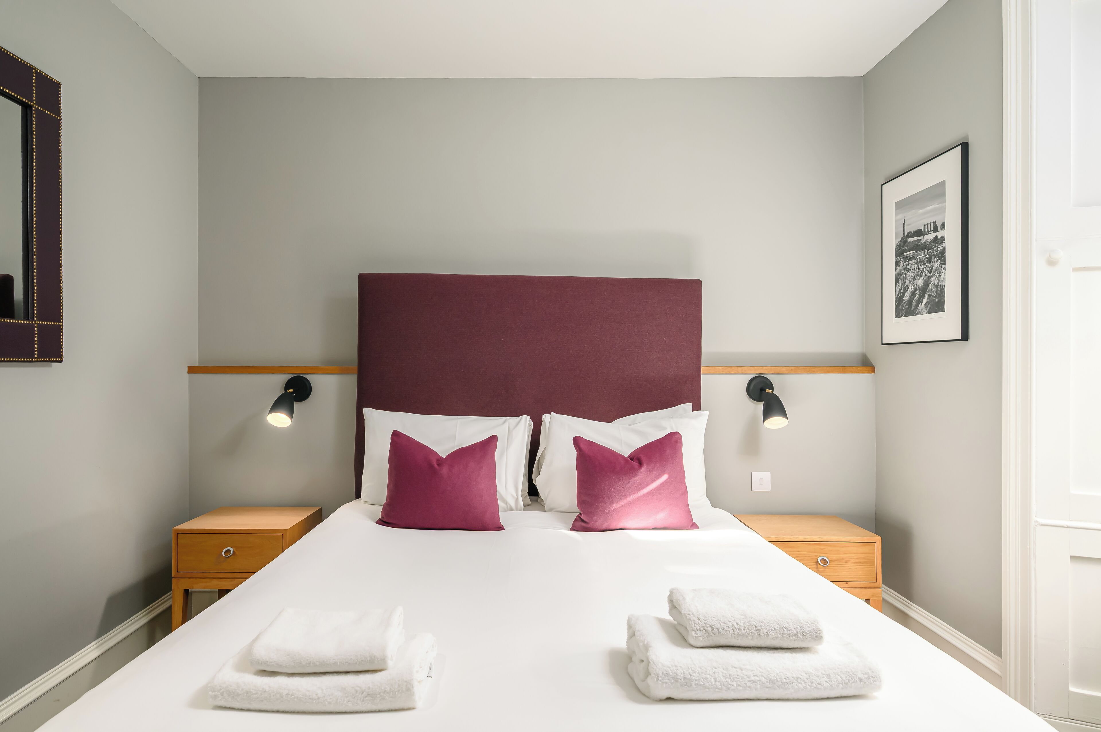A neatly made bed with white and pink pillows, two bedside tables with lamps, and a framed picture on the wall.
