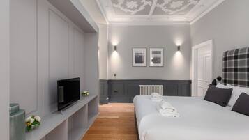 Una habitación de hotel moderna con una cama grande, un televisor de pantalla plana, un estante empotrado con objetos decorativos y un techo con diseños intrincados.