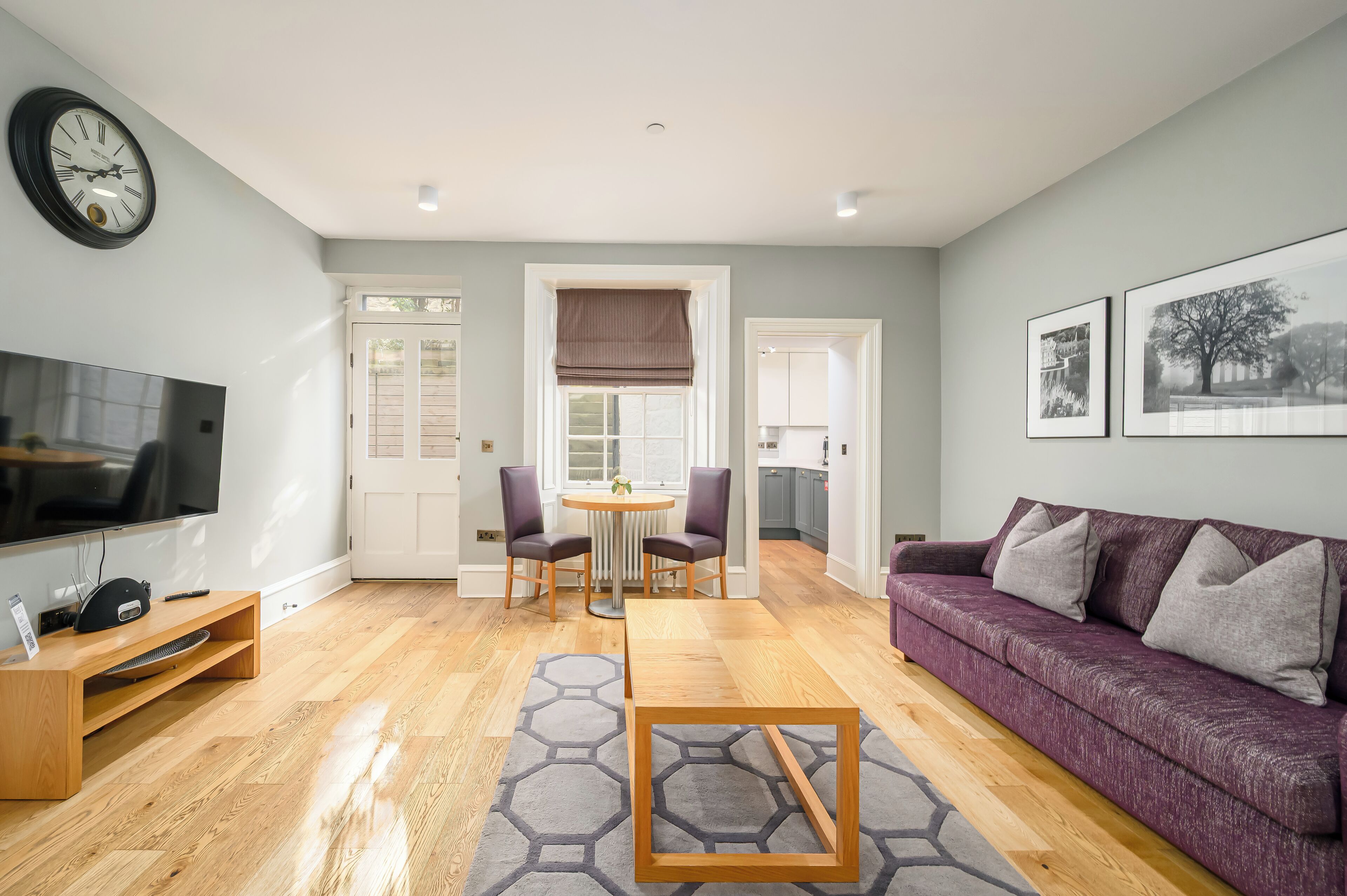 Un salon moderne avec une table basse en bois, un canapé violet, un téléviseur et un coin repas comprenant des chaises et une table.