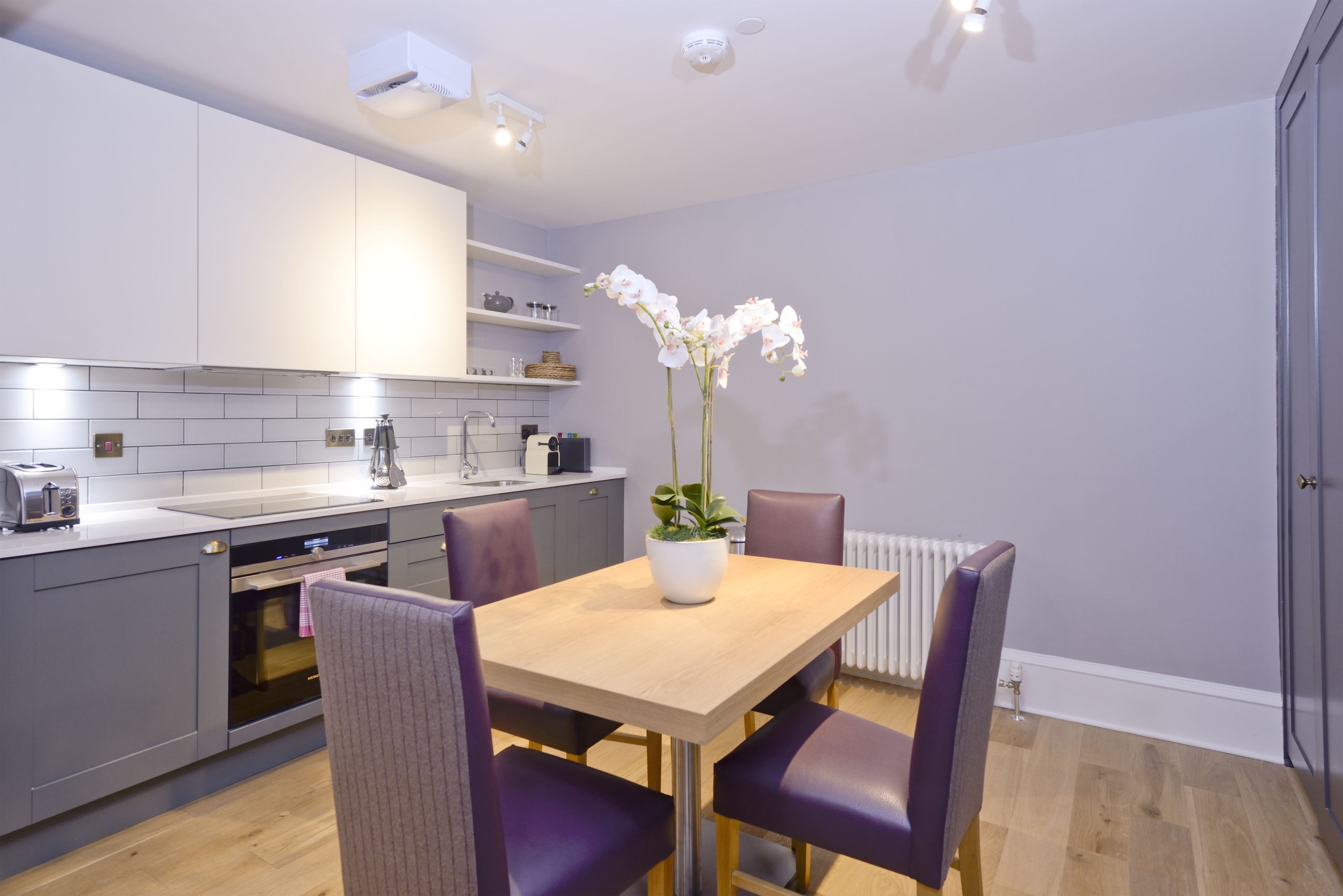 A modern kitchen with grey cabinets, a wooden dining table, and purple chairs.