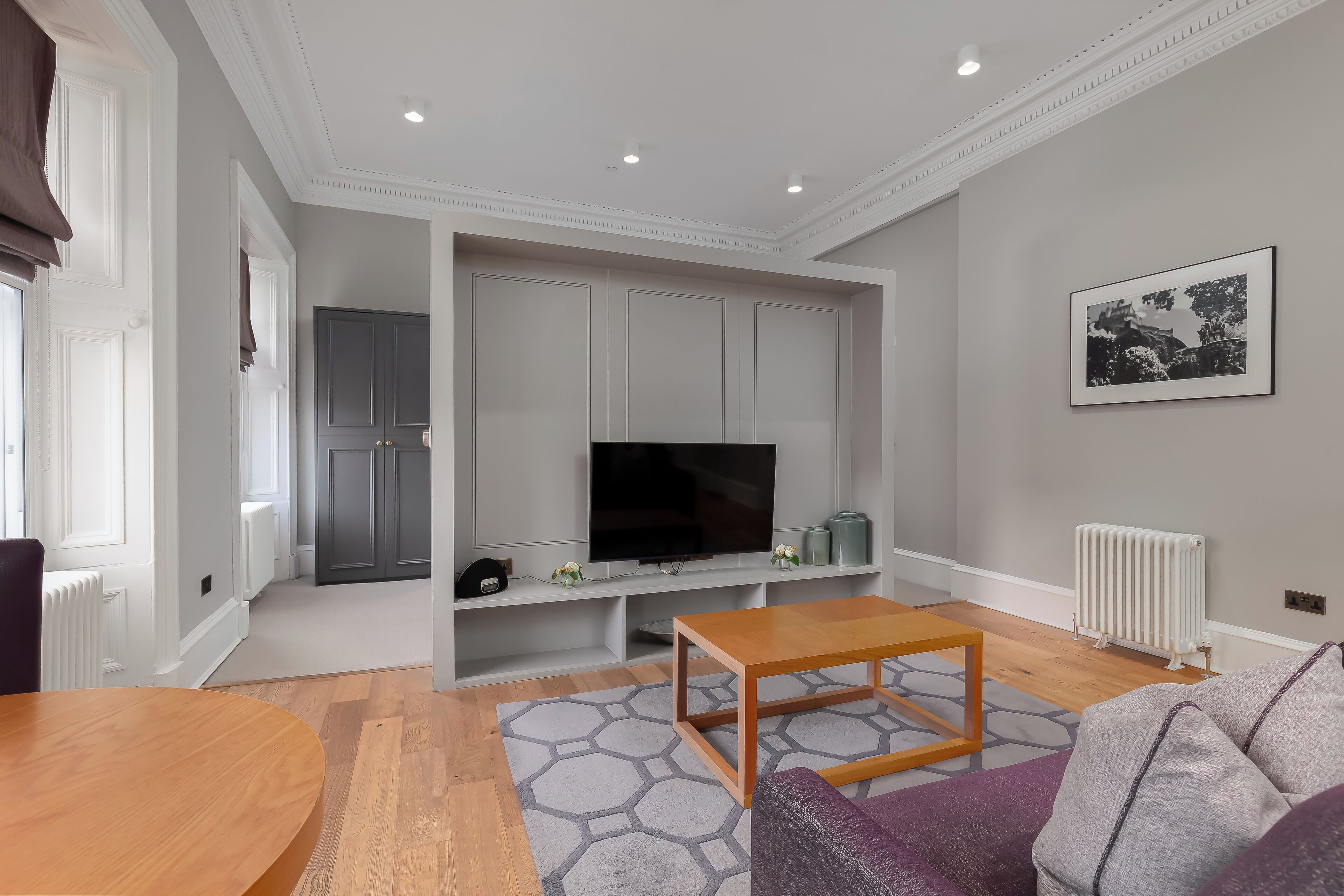 A modern living room with a television, wooden coffee table, grey sofa, and patterned rug.
