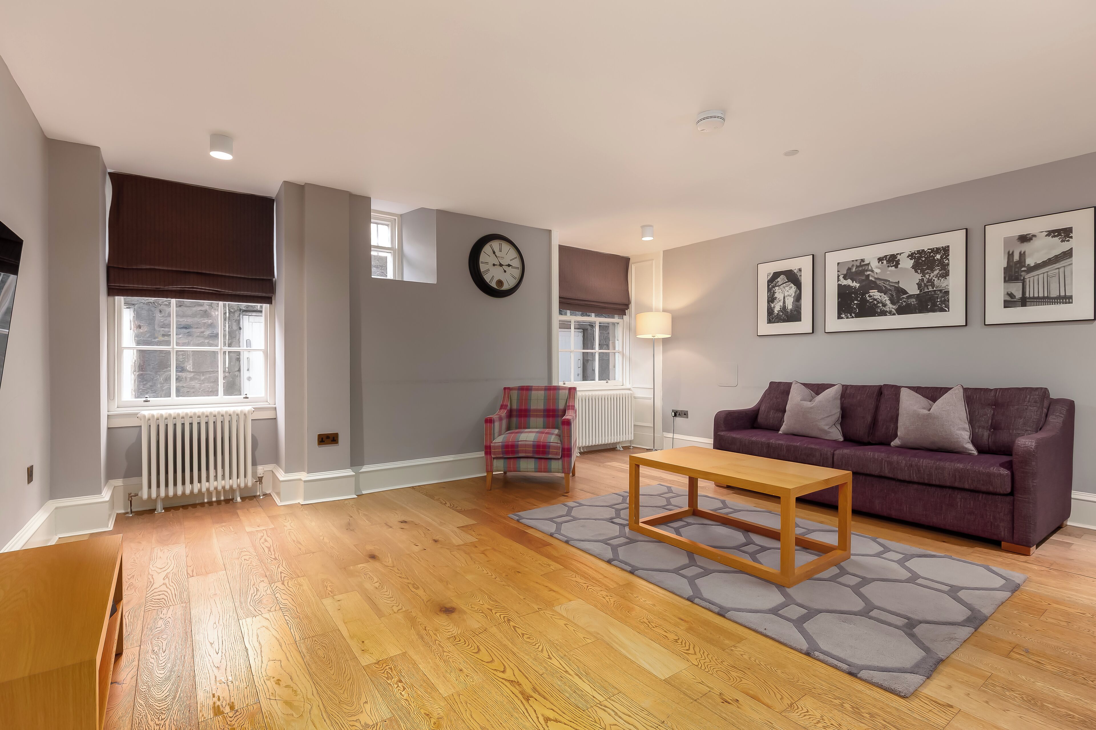 A living room with hardwood flooring, a purple sofa, a plaid armchair, and a wooden coffee table.