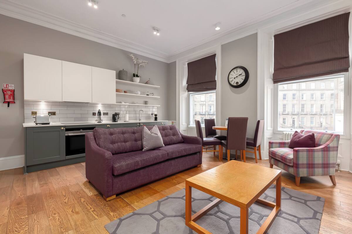 Una sala de estar moderna con un sofá púrpura, una mesa de centro de madera y una zona de comedor con sillas y una mesa.