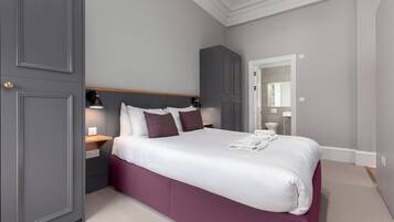 A neatly arranged bedroom with a large bed, a wardrobe, a nightstand, and a mirror.