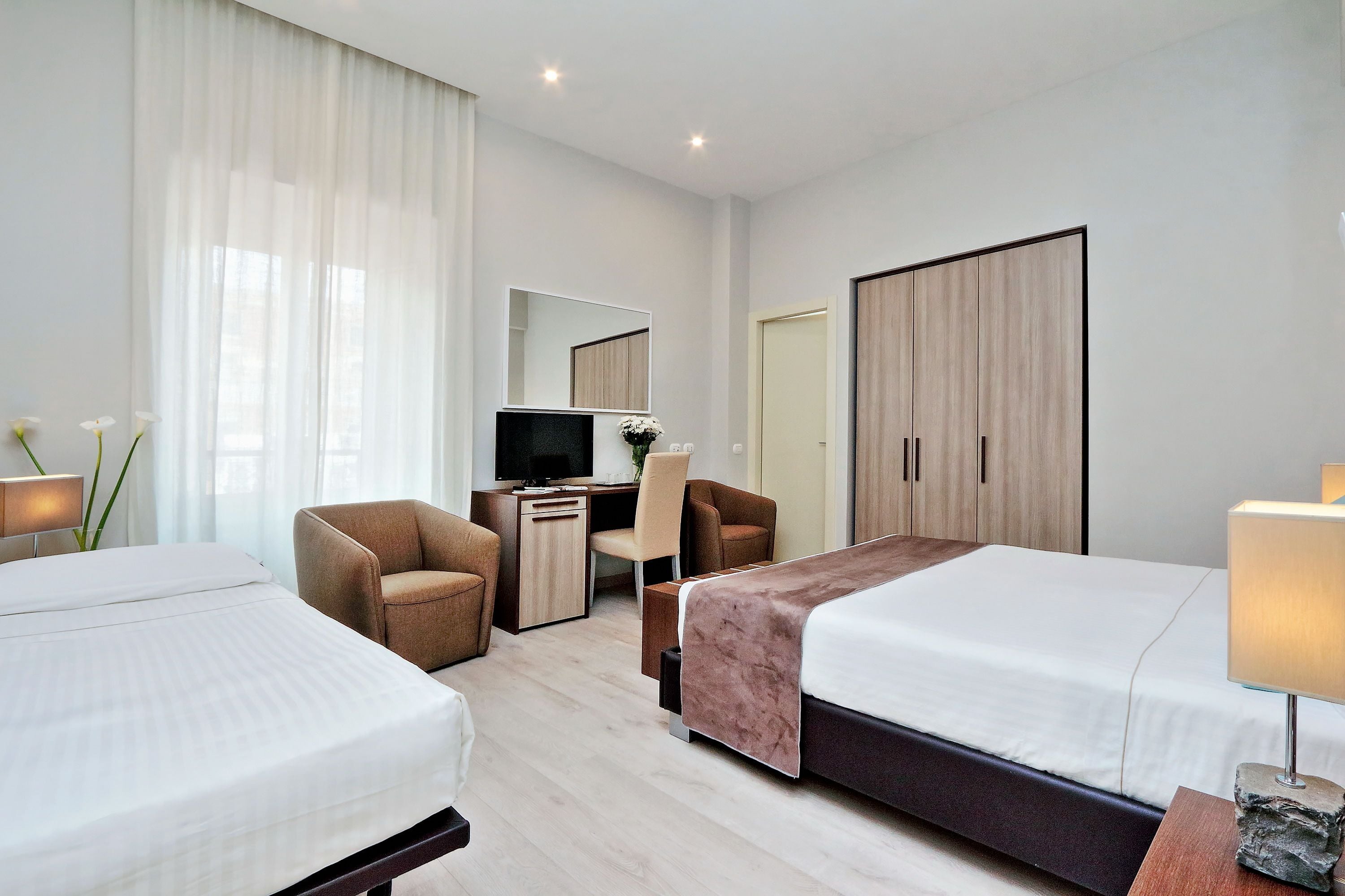 Habitación de hotel con dos camas, un escritorio, una silla, un televisor y un armario.