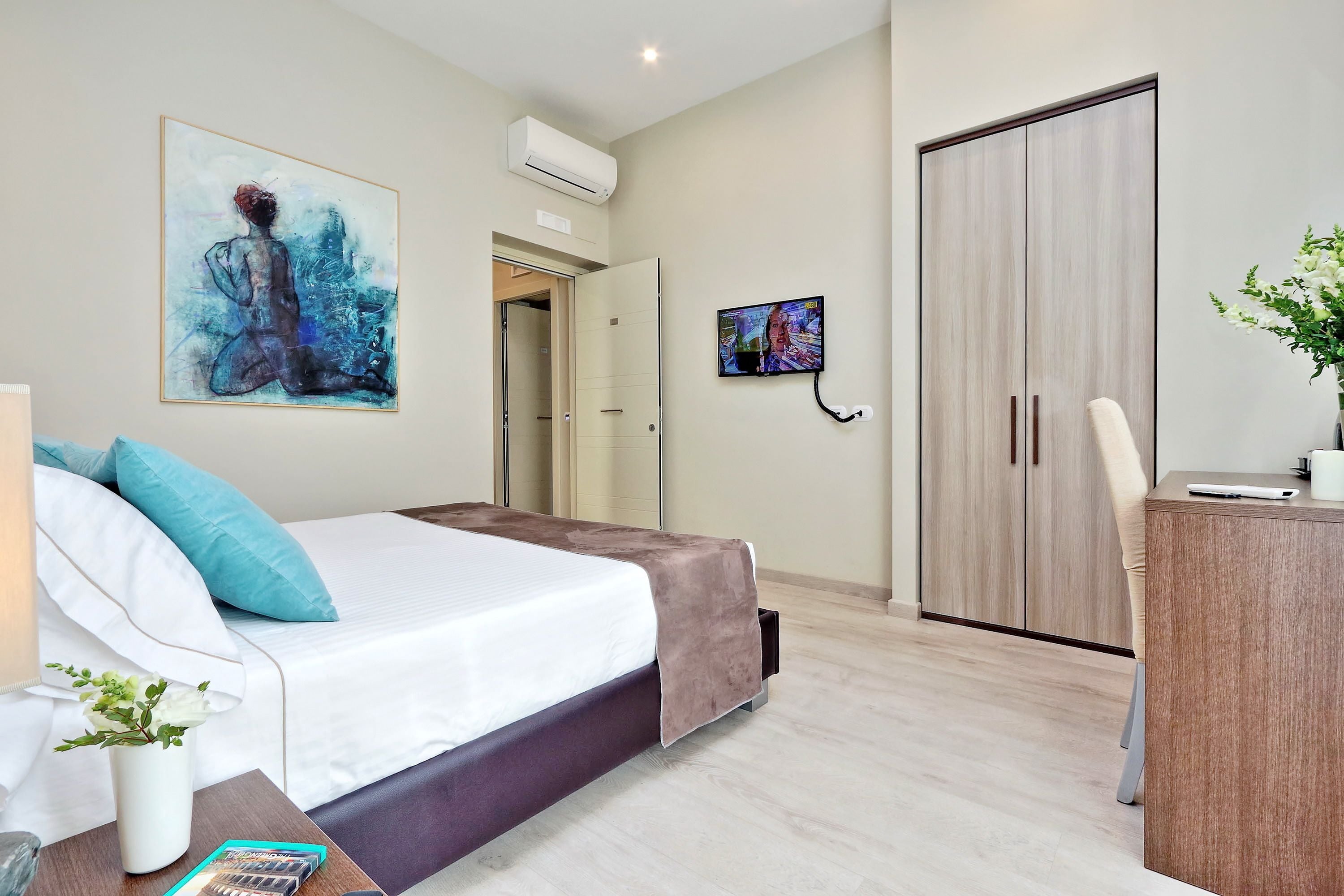 A modern hotel room with a bed, a desk, a TV, and a wardrobe.