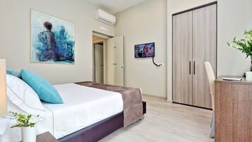 A modern hotel room with a bed, a desk, a TV, and a wardrobe.