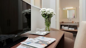 A hotel room with a TV, a newspaper, a vase with flowers, and a bathroom visible in the background. - Relais Servio Tullio (Rome)
