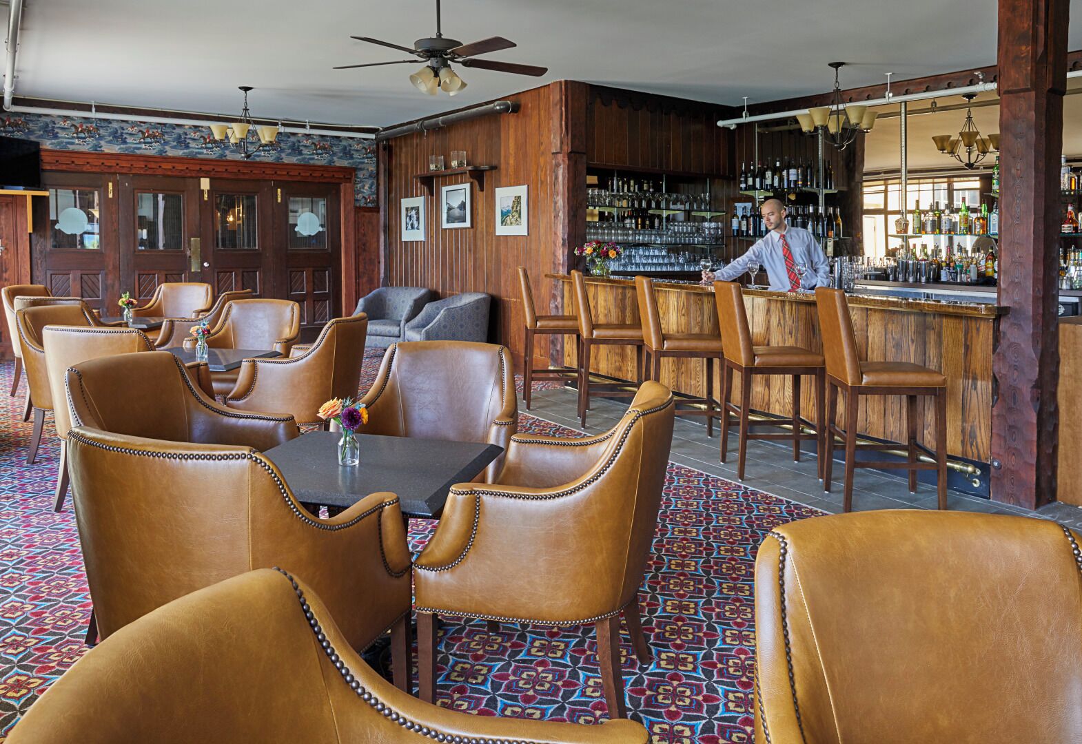A bar area with wooden furnishings, a bartender, and a patterned carpet.