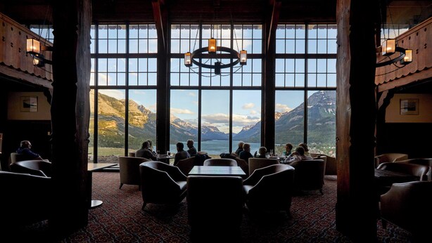 Une pièce dotée de grandes fenêtres, d’un lustre et où un groupe de personnes est assis autour d’une table.