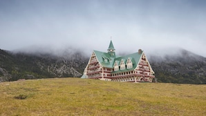 Un grand bâtiment à plusieurs étages, doté d’un toit végétalisé et d’une tour, entouré d’un champ verdoyant et de montagnes.