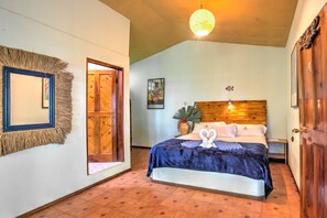 A bedroom with a bed, a wooden headboard, a nightstand, a wall-mounted mirror, and a door. - La Diosa Nature Lodge (Cahuita)