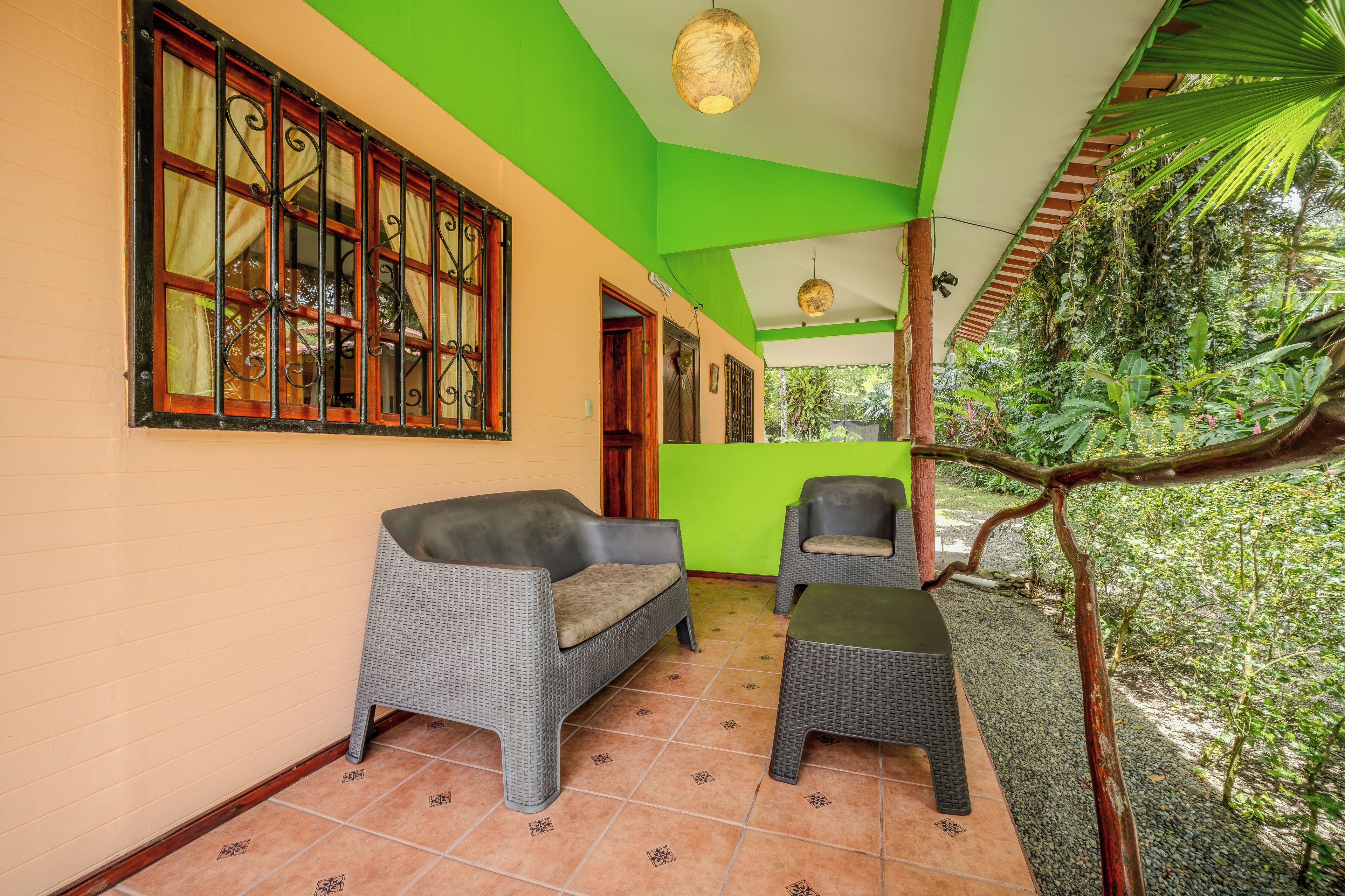 Une pièce avec un plafond vert, un canapé en osier, une petite table et une vue sur un jardin luxuriant.