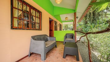 Une pièce avec un plafond vert, un canapé en osier, une petite table et une vue sur un jardin luxuriant.