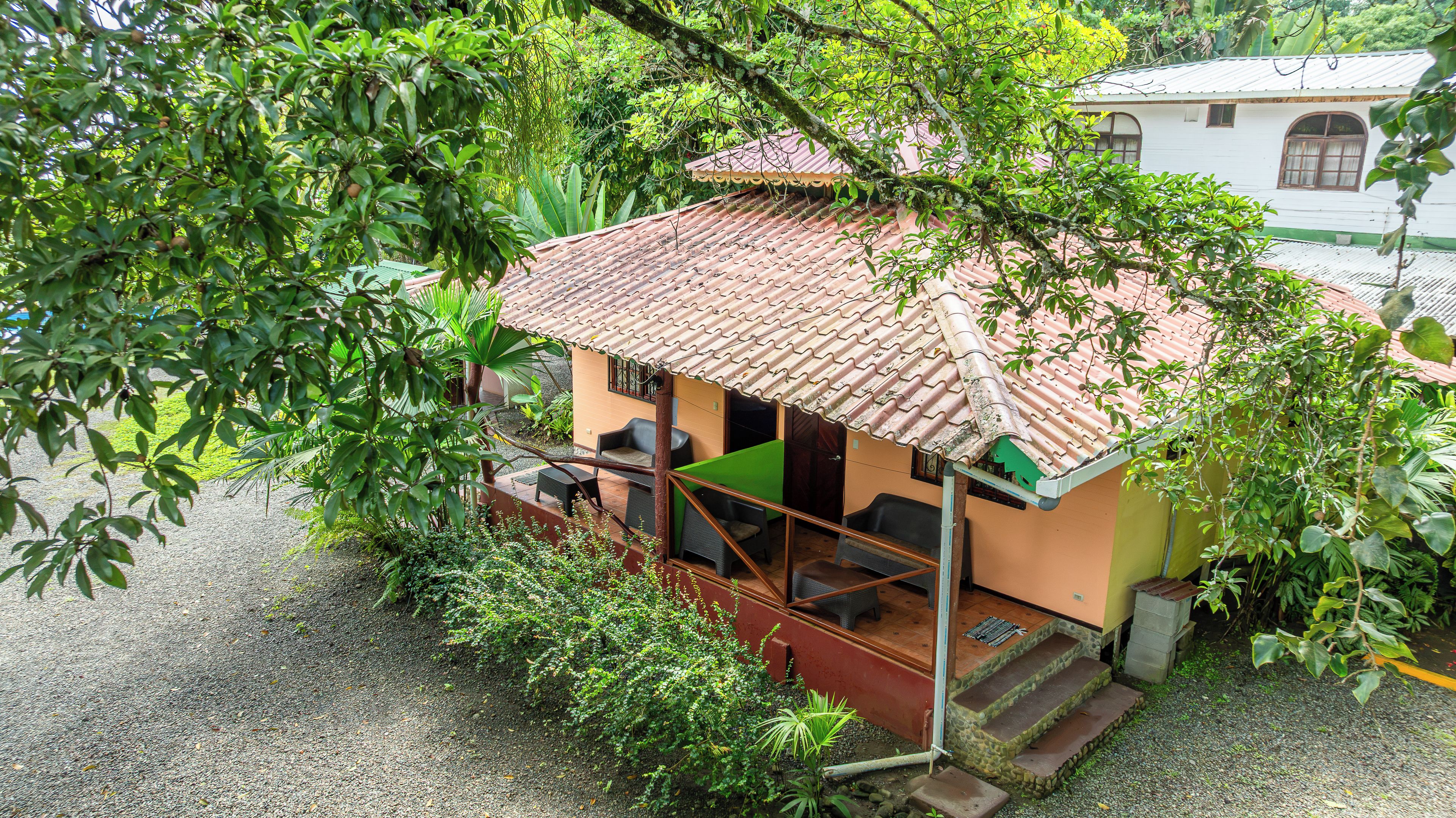 A small house with a tiled roof, a porch with seating, and a gravel ground.