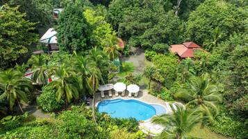 A pool surrounded by lush greenery, with a red-roofed building and a white structure in the background.