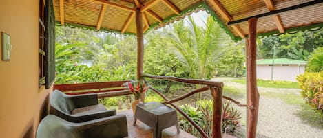 Un espace extérieur abrité, aménagé avec des sièges, et un escalier en bois qui mène à un jardin.