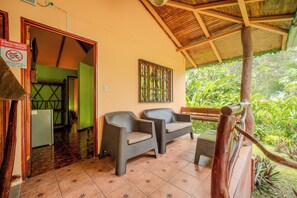 A covered outdoor seating area with wicker furniture, a wooden railing, and a view of lush greenery. - La Diosa Nature Lodge (Cahuita)