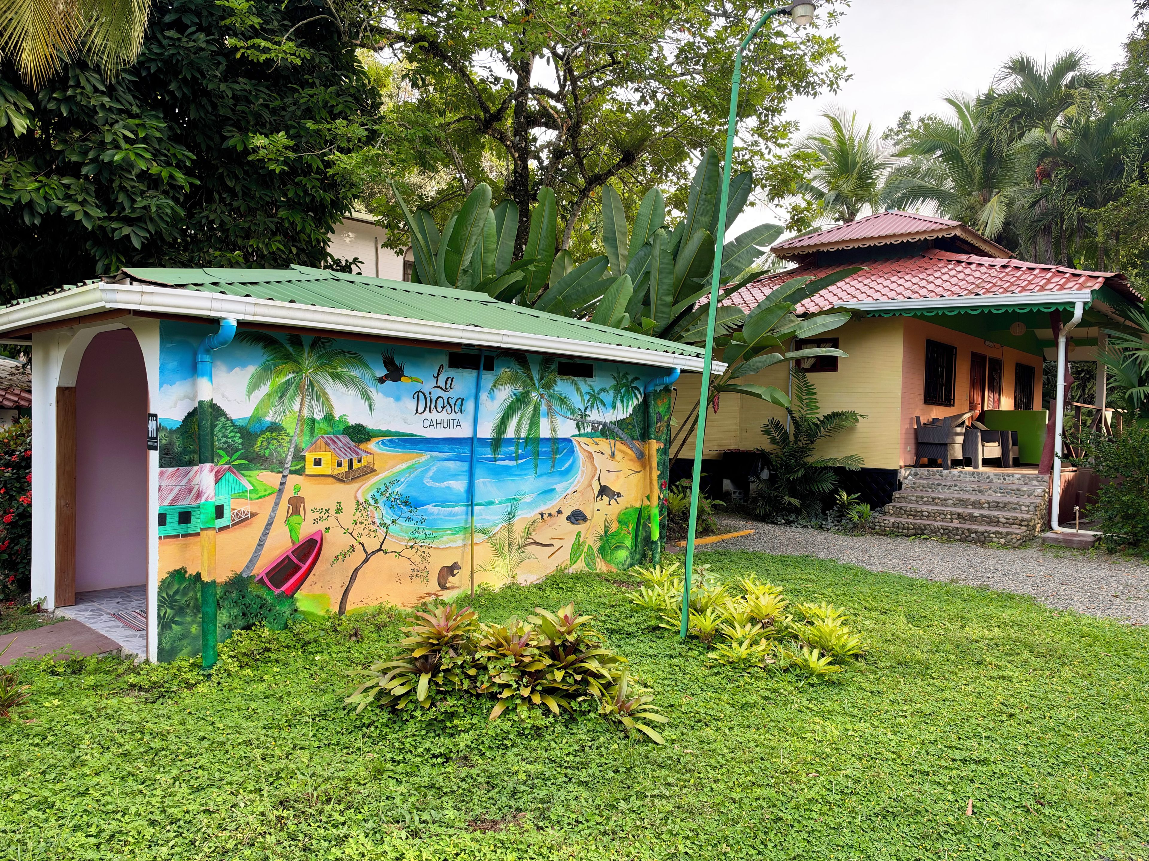 Un edificio con un mural que representa una escena de playa, un área de estar techada al aire libre y una escalera que conduce a otro edificio.
