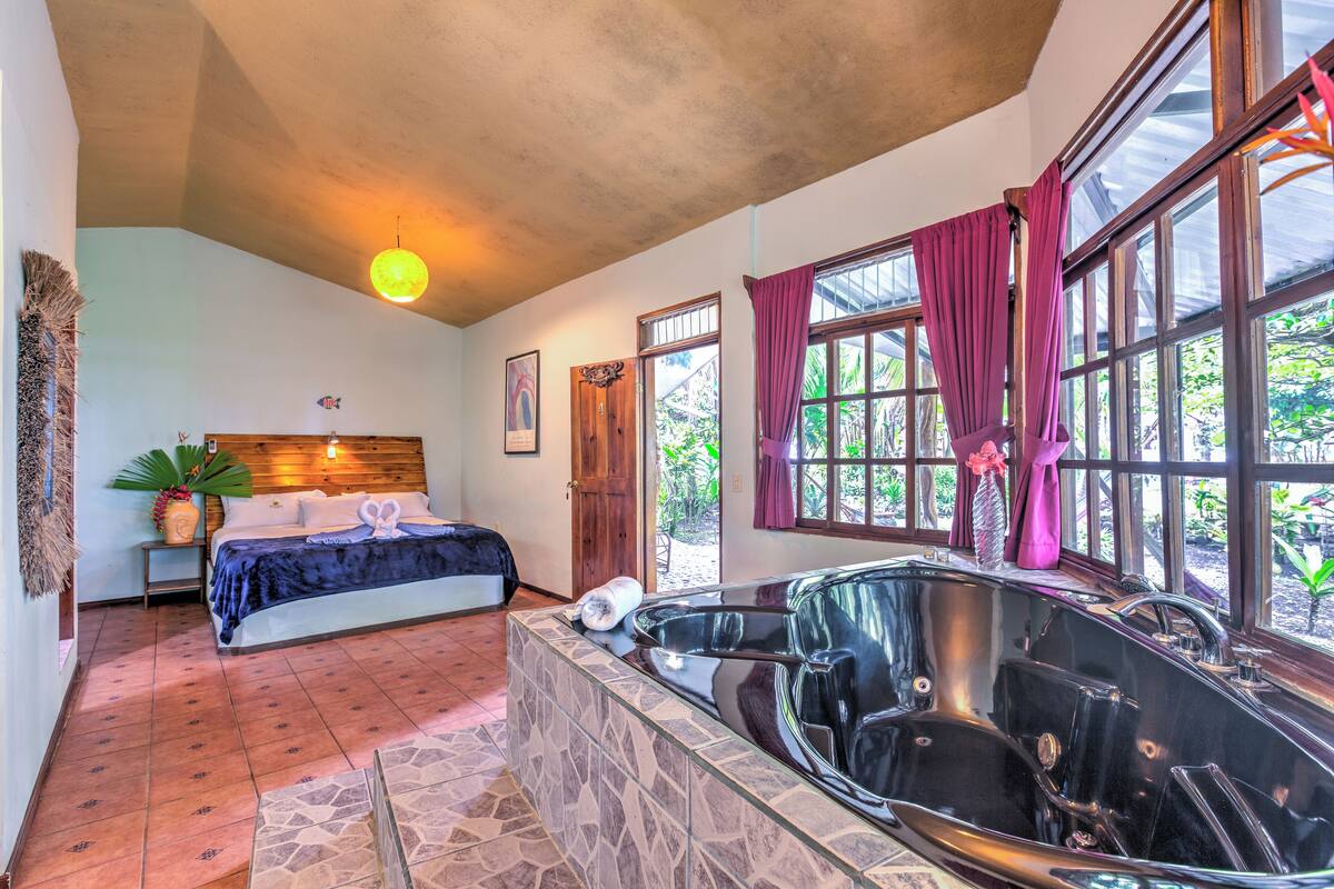 A bedroom with a large bed, a bathtub, and a window with curtains.
