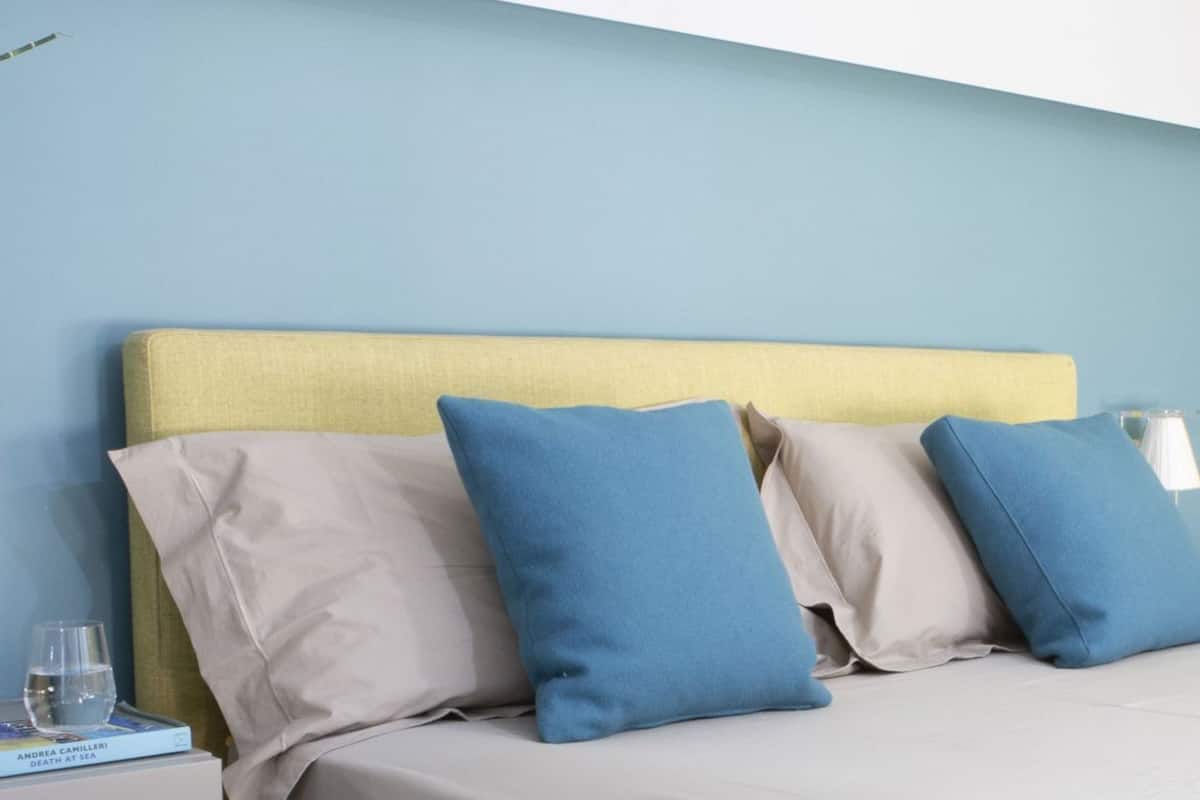A bed with a yellow headboard, beige bedding, and blue pillows.