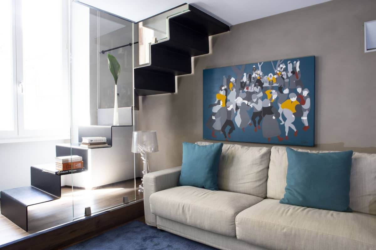 A modern living room with a sofa, a painting, and a staircase.