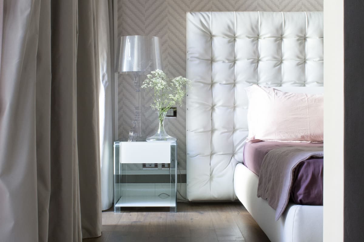 A bedroom with a tufted headboard, a bedside table with a lamp, and a vase with flowers.