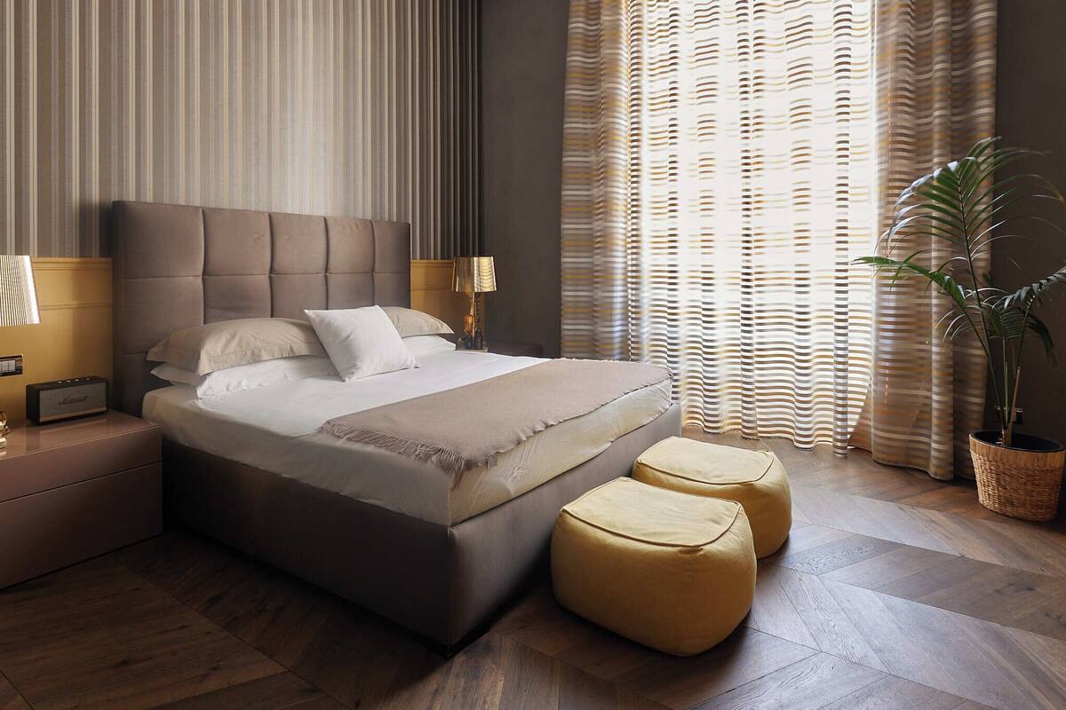 A modern bedroom with a large bed, two bedside tables, a lamp, and a potted plant.