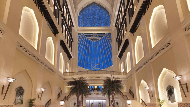 A grand lobby with a high ceiling, a central staircase, and a large blue patterned skylight. - Bab Al Qasr Residence (Abu Dhabi)