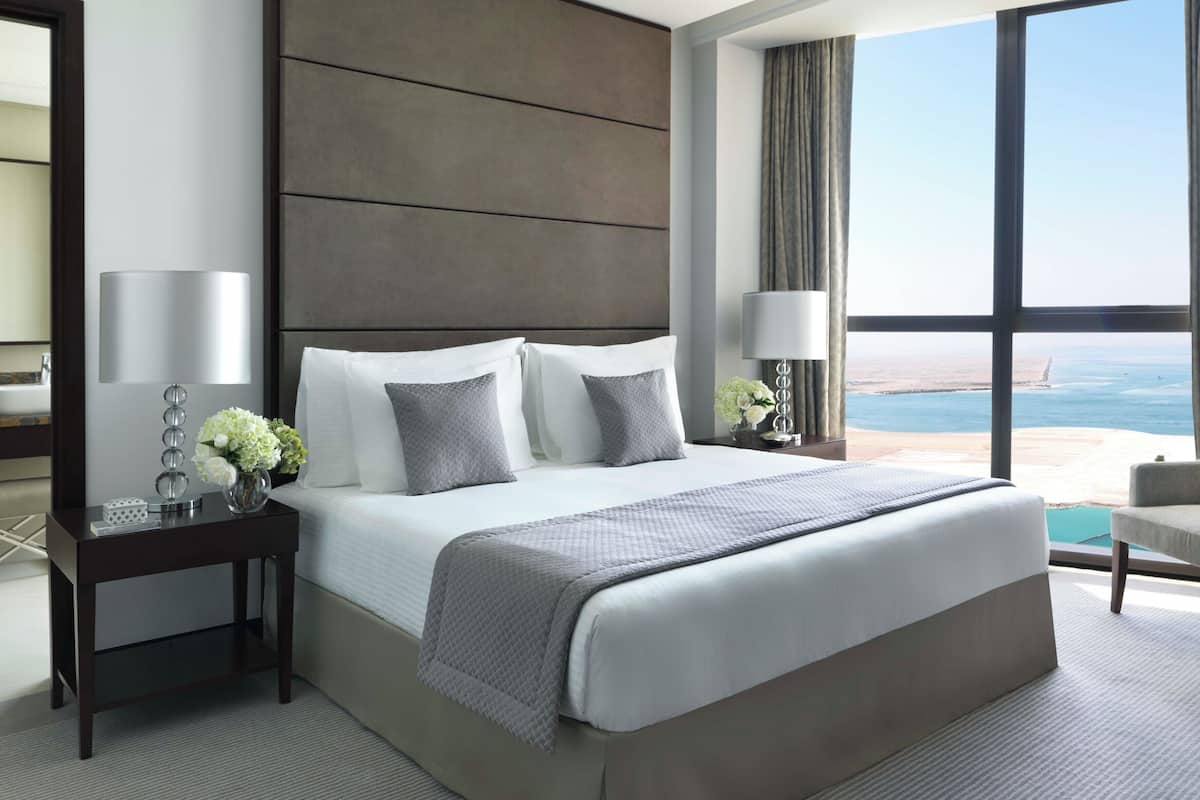 Une chambre d’hôtel moderne dotée d’un grand lit, de deux tables de chevet, d’une commode, d’une vue sur l’océan et d’un balcon.