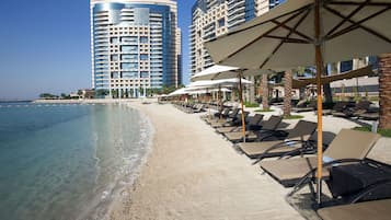 Na praia, areia branca, espreguiçadeiras, guarda-sóis