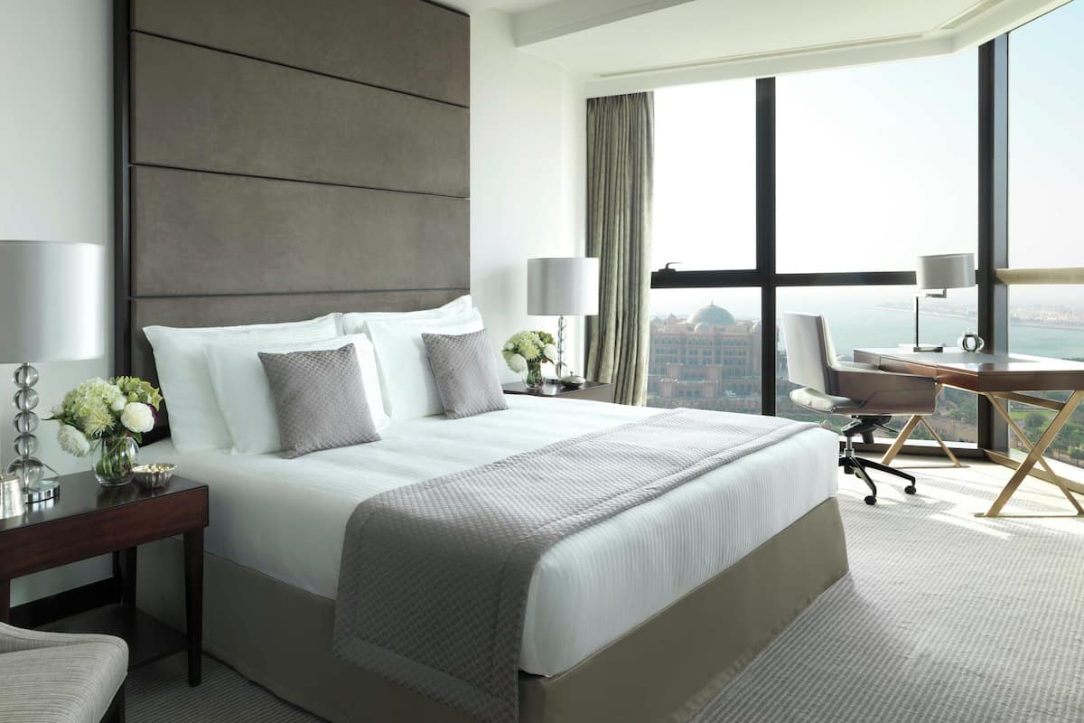 Une chambre d’hôtel avec un grand lit, un bureau, une chaise et une vue sur le paysage urbain, grâce à de grandes fenêtres.