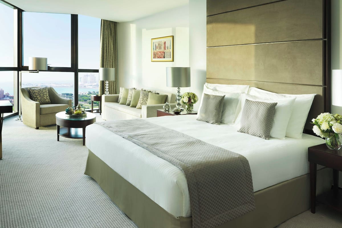 Une chambre d’hôtel avec un grand lit, deux canapés, un bureau et une vue sur la ville.