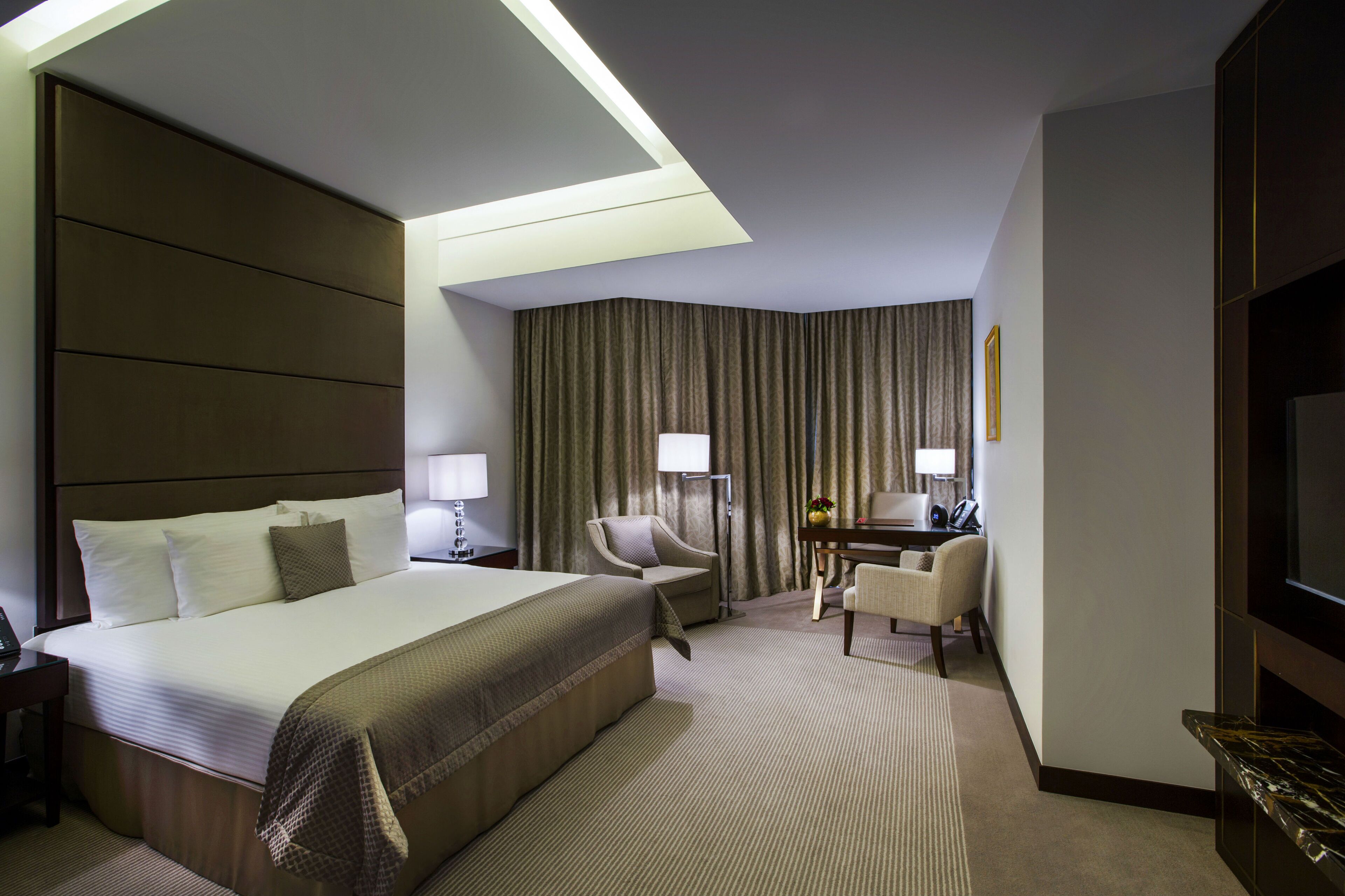 A hotel room with a large bed, a desk with a chair, a television, and a window with curtains.