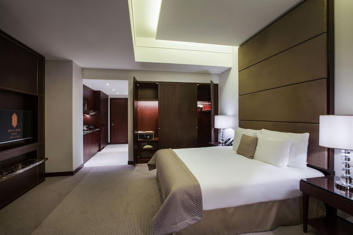 Une chambre d’hôtel avec un grand lit, une télévision, un bureau avec une lampe, une armoire et une salle de bain visible à travers une porte ouverte.
