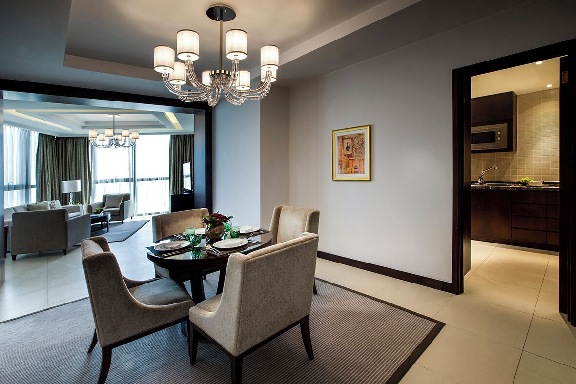 Habitación de hotel moderna con comedor, candelabro, un cuadro enmarcado y vista hacia la cocina.