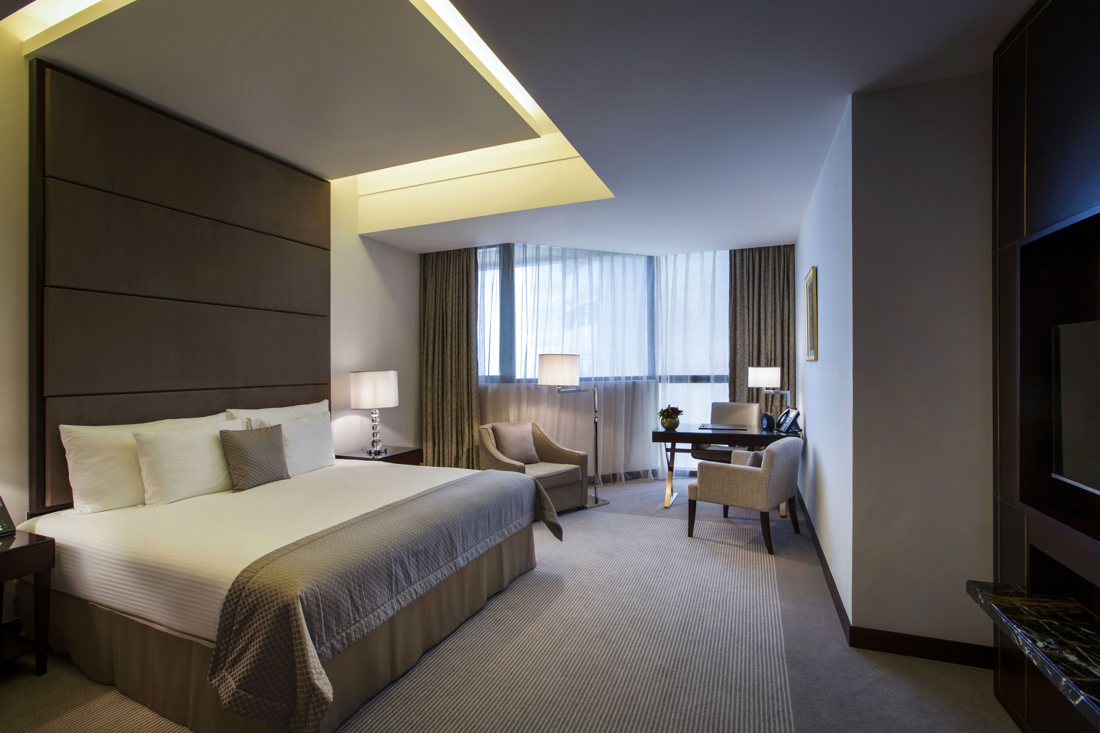 Une chambre d’hôtel avec un grand lit, un bureau, une chaise, une télévision et une fenêtre avec des rideaux.