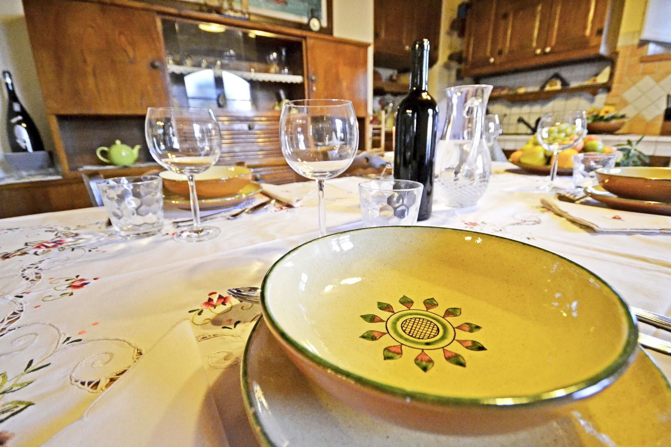 Una mesa de comedor con mantel floral, un cuenco decorativo, copas de vino y una botella de vino.