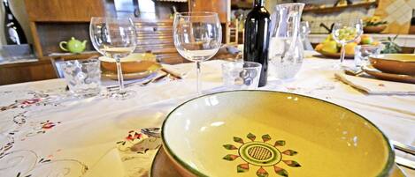Una mesa de comedor con mantel floral, un cuenco decorativo, copas de vino y una botella de vino.