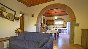Un salon avec un canapé, un coin repas avec une table et des chaises, et une cuisine visible à travers une arche.